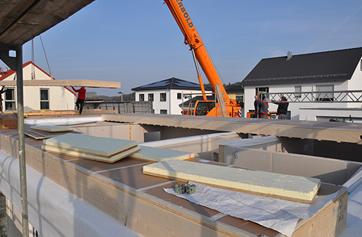 Referenz Baustelle Baustellenbild eines Holzhauses , ein Kran bringt gerade die Decke des ersten Geschosses auf